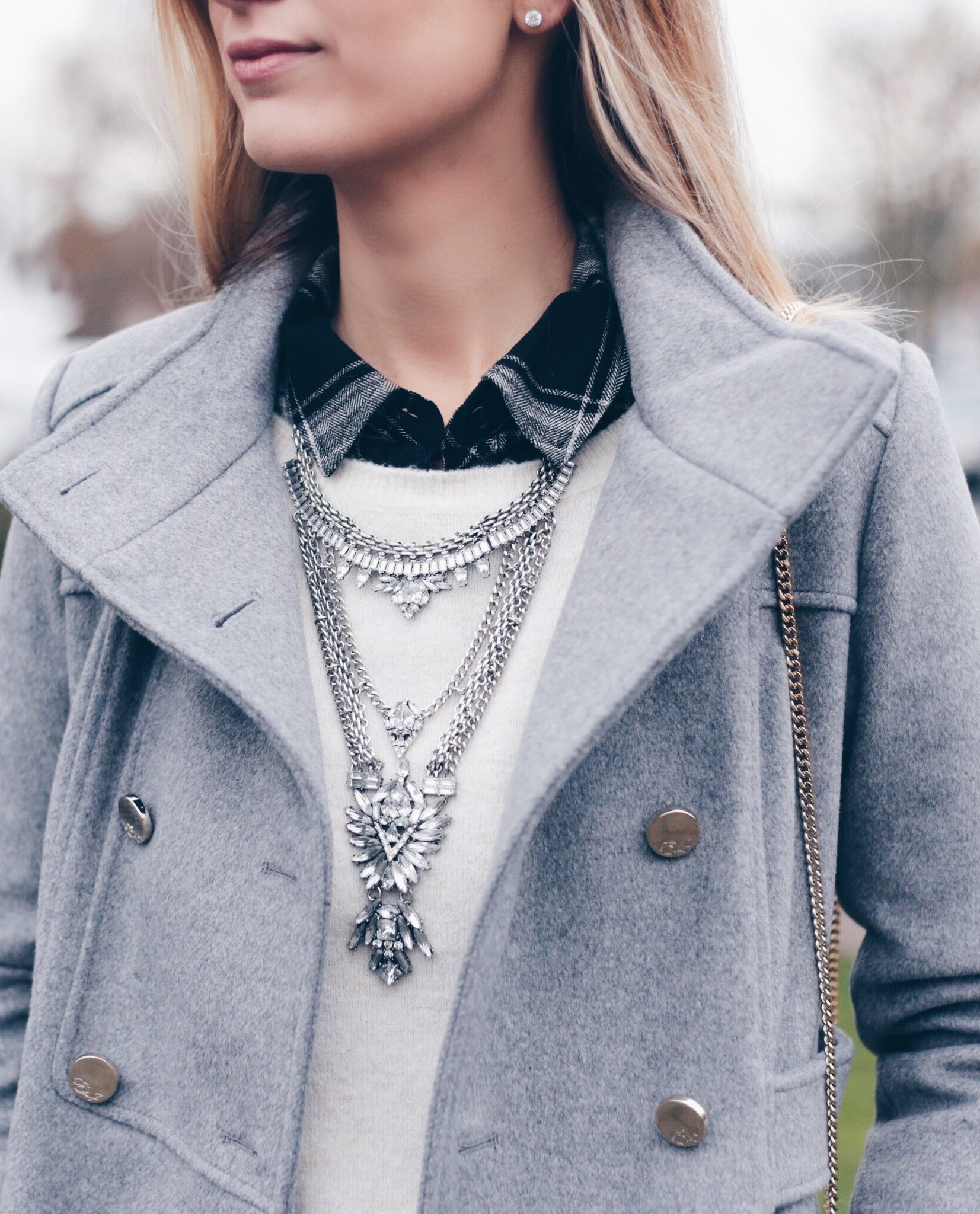 gray women's military coat with statement bib necklace over white crewneck sweater