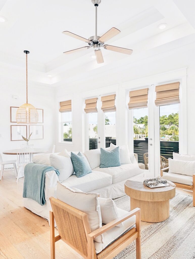 Bright and airy coastal living room featuring timeless neutral capsule home decor staples, including a white slipcovered sofa, woven accent chairs, and natural wood finishes.
