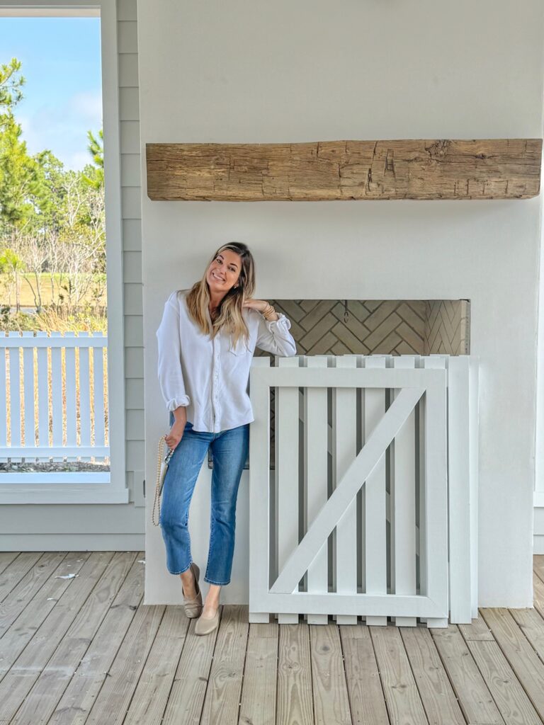 Outdoor fireplace featuring a high wood mantel and a white decorative wood gate, on a covered porch.