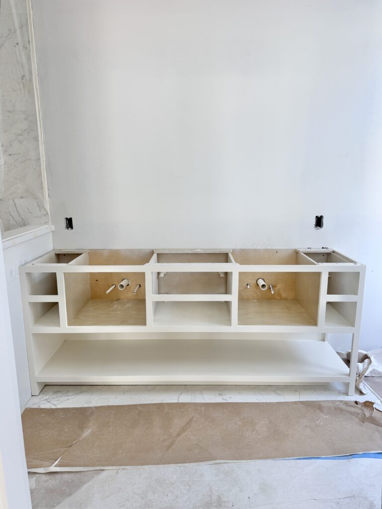 Close-up of white double-sink vanity cabinet with open plumbing access, part of a bathroom renovation for a new Florida home build.
